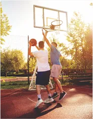 Two men playing basketball on a court with the sun shining at AIPL DreamCity Ludhiana