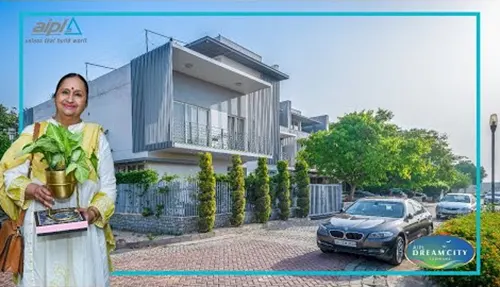 Woman holding a plant in front of a house at AIPL DreamCity township project in Ludhiana, Punjab